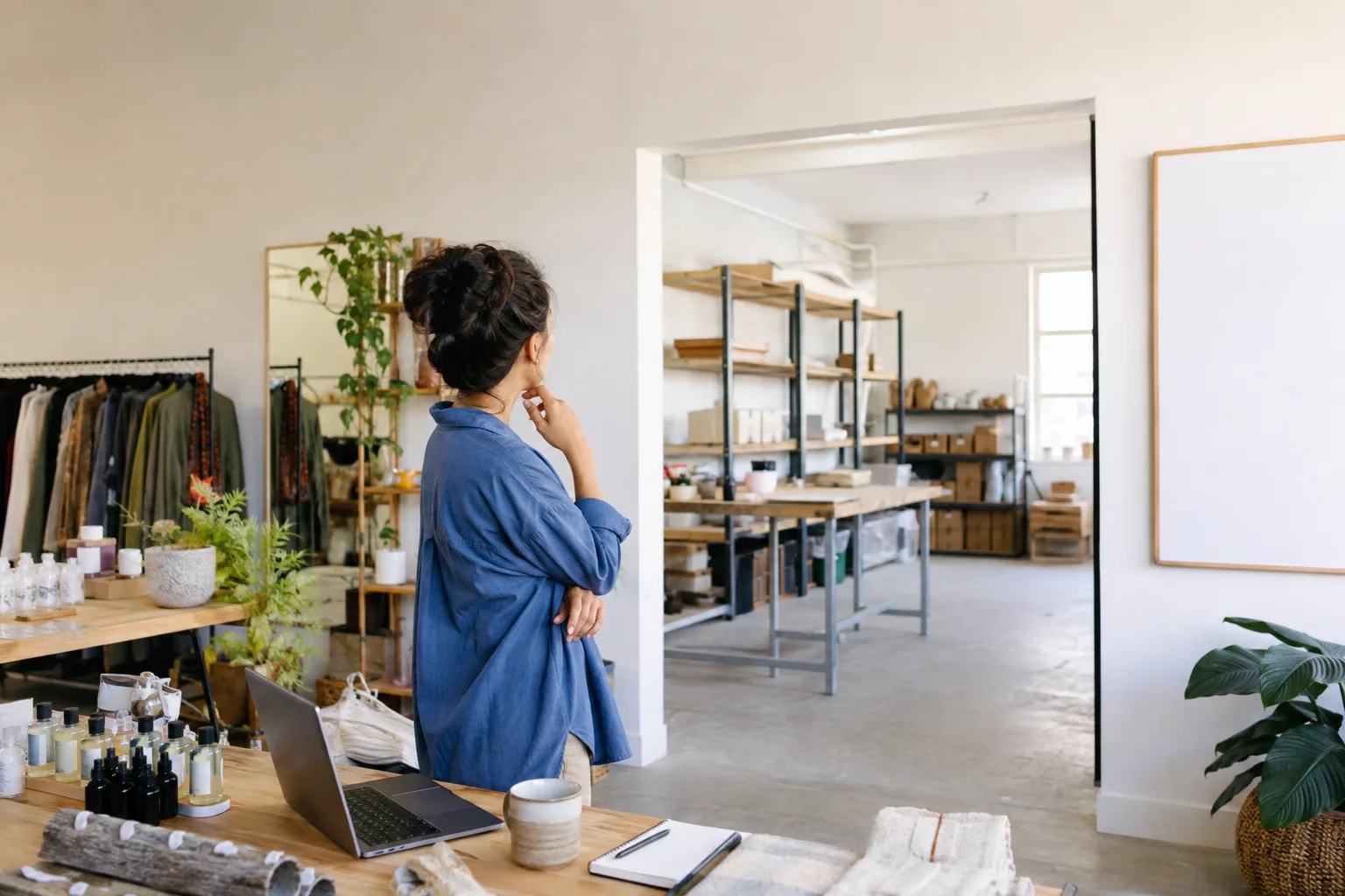 A small-business owner looks from a working shop toward a bright adjoining expansion space